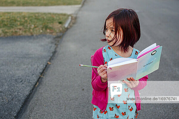 Ein vom Wind verwehtes kleines Mädchen geht die Straße entlang und macht sich Notizen in einem Tagebuch