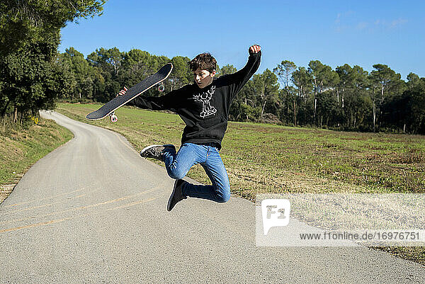 Action shot of a young skater teen male jumping high on a hill road