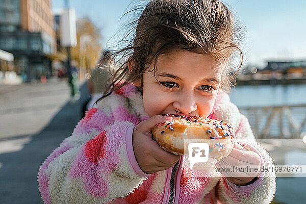 Junges Mädchen isst Donut mit Streuseln im Freien