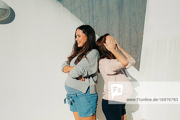 Zwei schwangere Frauen stehen an einer Wand an einem sonnigen Sommertag