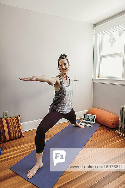 smiling woman in yoga clothes does yoga with help of laptop computer