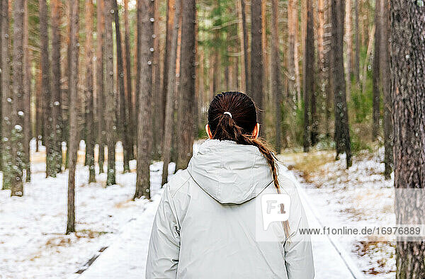 Rückansicht einer Frau mit einem Zopf im Haar  die durch einen verschneiten Wald geht.