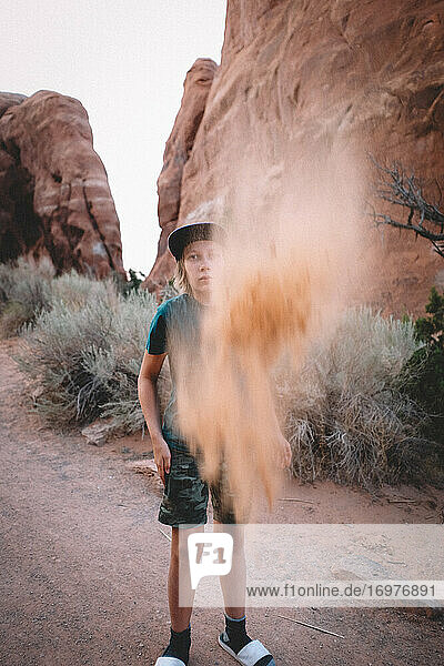 Junge wirft Sand in die Luft  umgeben von Sandstein und Wüste