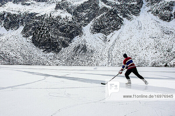Unbekannter Eishockeyspieler beim Schlittschuhlaufen auf einem zugefrorenen See in der Nähe eines Berges