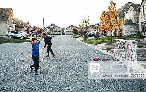 Zwei Jungen spielen Streethockey in einer Wohnstraße im Herbst.