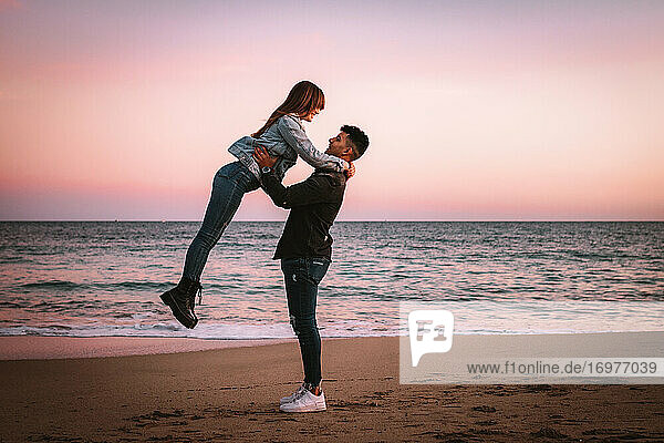 Boy Lifting His Girl On The Beach At Sunset