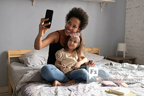 Fröhliche ethnische Mutter mit Tochter  die einen Videoanruf auf dem Smartphone macht