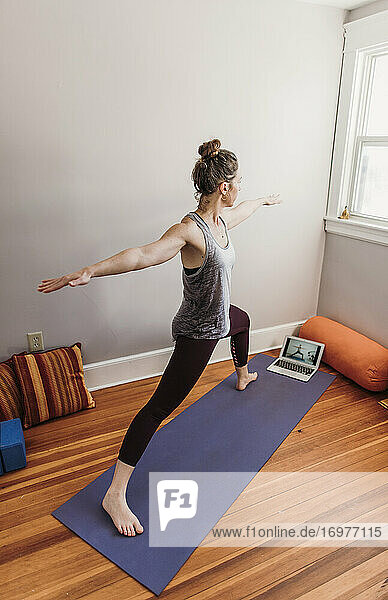 fit woman in her home practices yoga in front of a computer