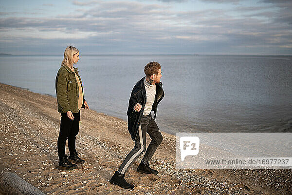 Young hipster couple throwing stones into lake