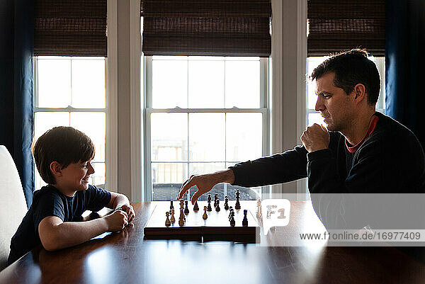 Vater und Sohn sitzen an einem Tisch in einem Haus und spielen eine Partie Schach.