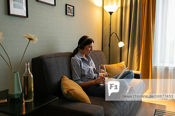 Junge Frau mit einem Glas Wein am Laptop zu Hause