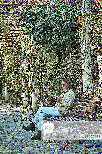 Relaxed young woman sitting on a bench using cell phone