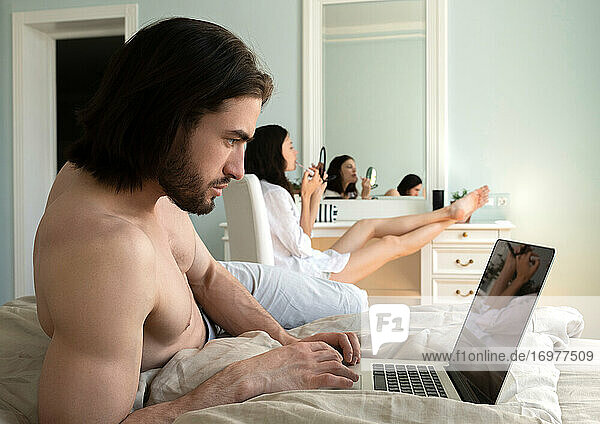 Der Mann arbeitet am Computer  während seine Frau sich schminkt