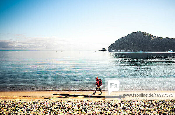 Woman walking down sandy beach with backack with ocean behind her