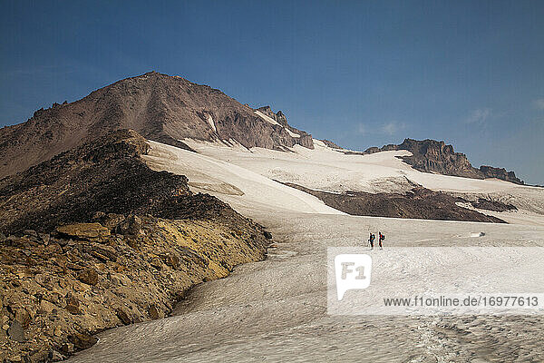 Two hikers climb towards the summit of Glacier Peak at dawn.