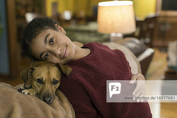 Biracial tween looking at camera while leaning against small brown dog