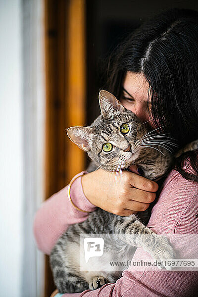 Frau umarmt eine Katze auf ihren Armen. Katze schaut in die Kamera