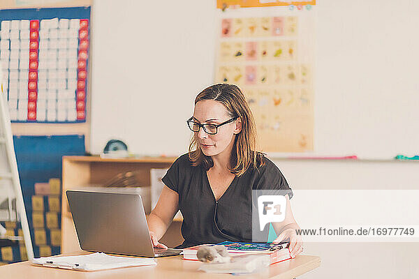 Eine Lehrerin tippt in ihrem Klassenzimmer auf ihrem Laptop.