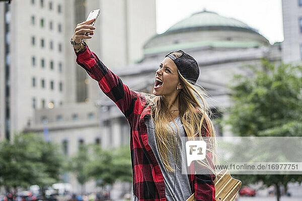 Stylische Städterin mit Skateboard macht ein Selfie in der Innenstadt