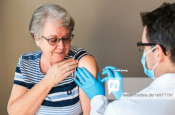 Older woman getting injected with a vaccine by doctor in upper arm.