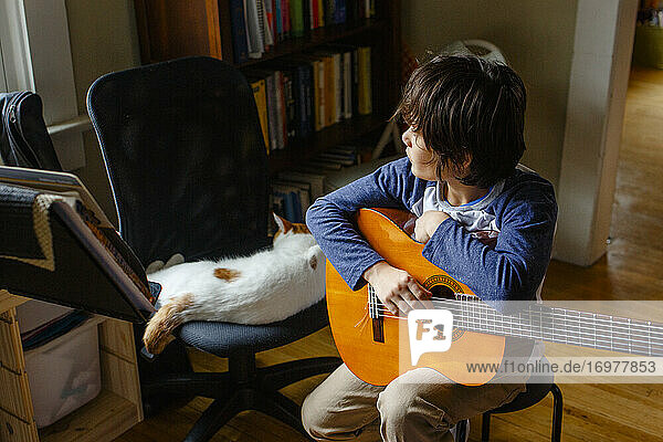 Ein Junge schaut aus dem Fenster und hält eine Gitarre neben einer schlafenden Katze