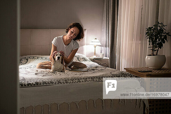 Frau streichelt Hund auf dem Bett