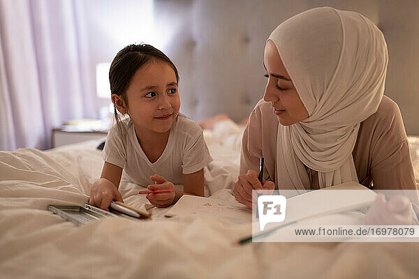 Muslim mother and daughter drawing on bed