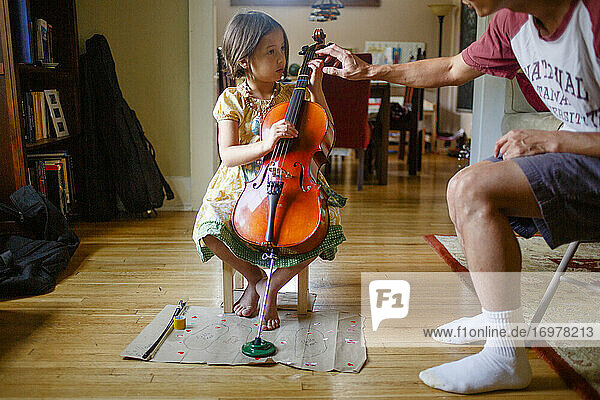 Ein Vater beugt sich vor  um einem kleinen Mädchen beim Üben des Cellospiels zu helfen