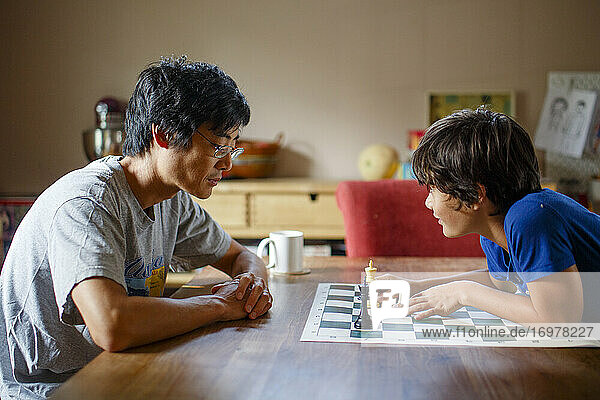 A boy makes chess move while playing with father at dining room table