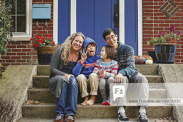 Eine glückliche Familie sitzt lächelnd auf der Treppe vor ihrem Haus zusammen
