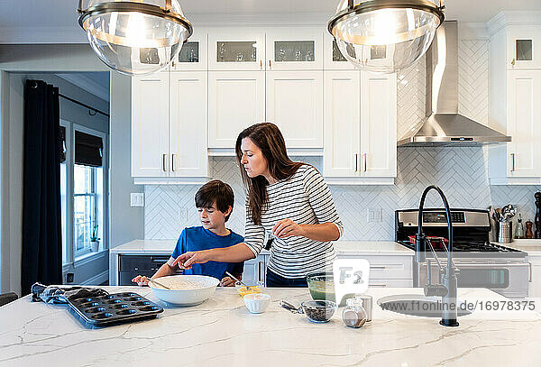 Mother and son making muffins together in a modern white kitchen.