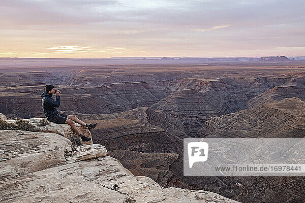 Man drinks coffee sitting on edge of cliff  Mexican Hat  Utah