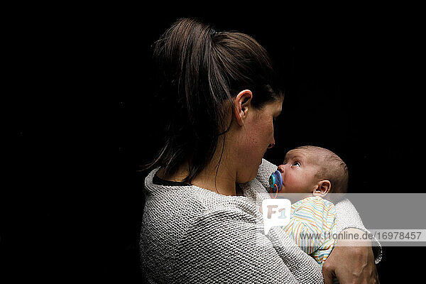 Seitenansicht der glücklichen Mutter kuscheln liebenswert neugeborenes Baby und genießen Momente der Mutterschaft gegen schwarzen Hintergrund