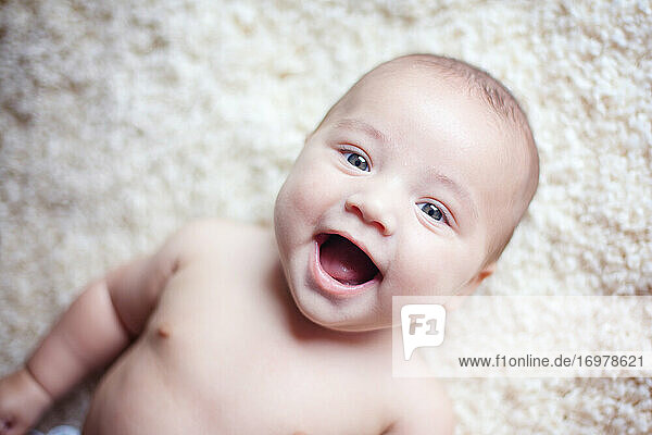 Baby boy laying on carpet and smiling big at the camera.