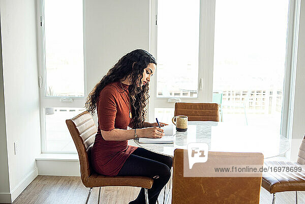 Frau sitzt am Tisch und schreibt in ein Notizbuch mit Kaffeebecher