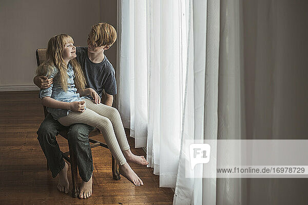 Siblings sitting on chair in studio with window light
