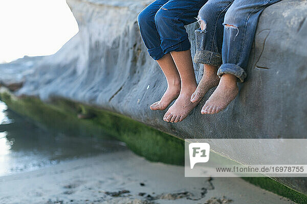 Brüder sitzen auf einem großen Felsen am Strand - Fokus auf ihre nackten Füße