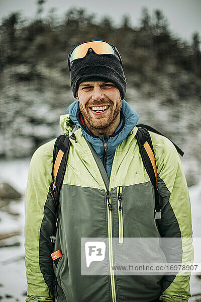 Porträt eines lächelnden Mannes in Winterjacke und Hut mit Rucksack