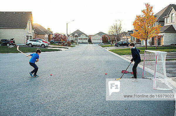 Zwei Jungen spielen Streethockey in einer Wohnstraße im Herbst.