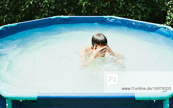 Junge in einem Schwimmbad  der ein Bad nimmt und mit den Fingern Wasser aus dem Gesicht entfernt.