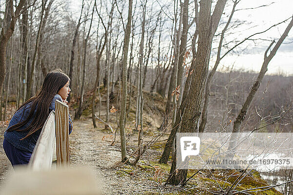 Ein Mädchen mit langen Haaren lehnt an einem Zaun und blickt auf ein bewaldetes Tal