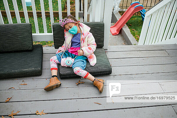 Little girl in crown slumped on deck tired from birthday party
