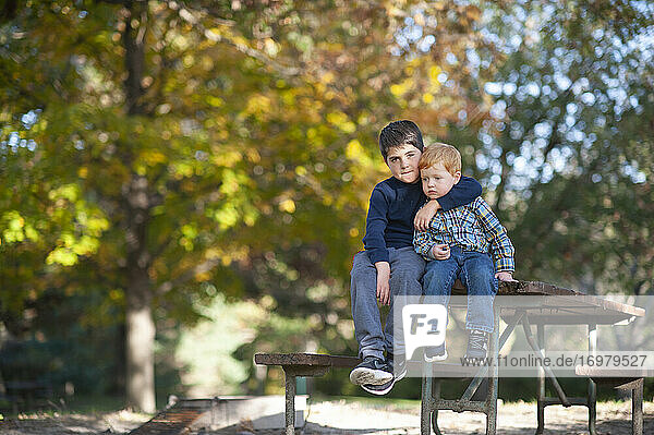 Big brother puts his arm around little brother sitting on picnic table