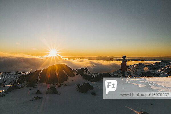 Junge Frau mit roter Jacke beobachtet den Sonnenuntergang am Horizont im Whakapapa Ski Resort  Neuseeland
