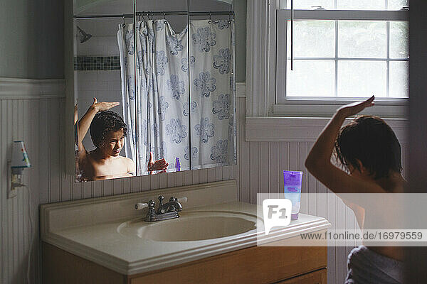 Ein in ein Badetuch eingewickelter Junge schaut in den Spiegel und trägt Haargel auf