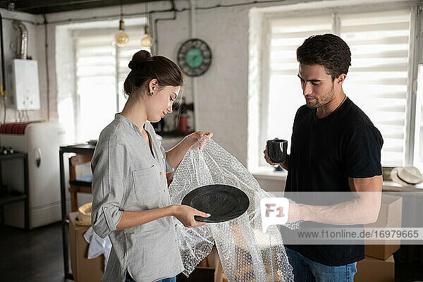 Young couple unwrapping dishware in new apartment