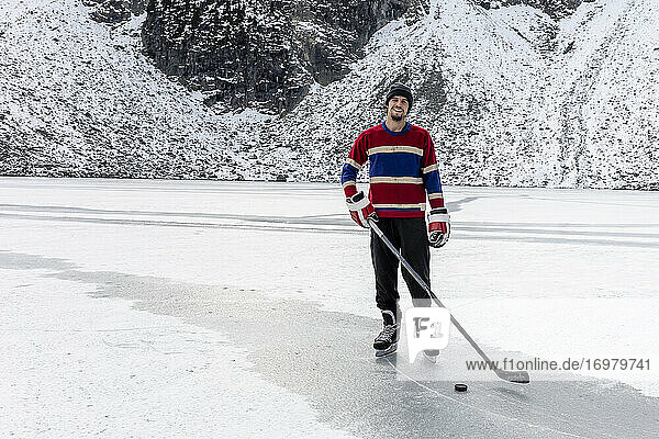Glücklicher Eishockeyspieler auf gefrorenem See mit Schläger und Puck  lächelnd
