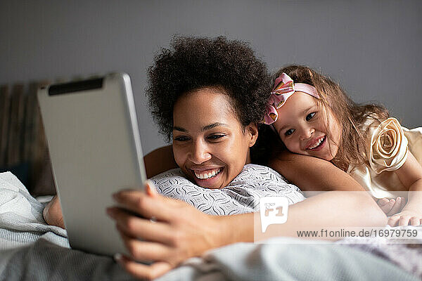 Gemischte Rasse Mutter und Tochter machen Videoanruf auf dem Bett