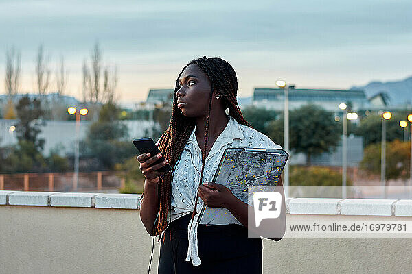 Junge afrikanische Studentin benutzt ihr Handy und hält einen Ordner
