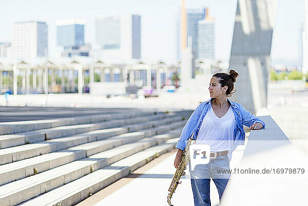 Woman with ponytail standing while posing with a saxophone outdoors